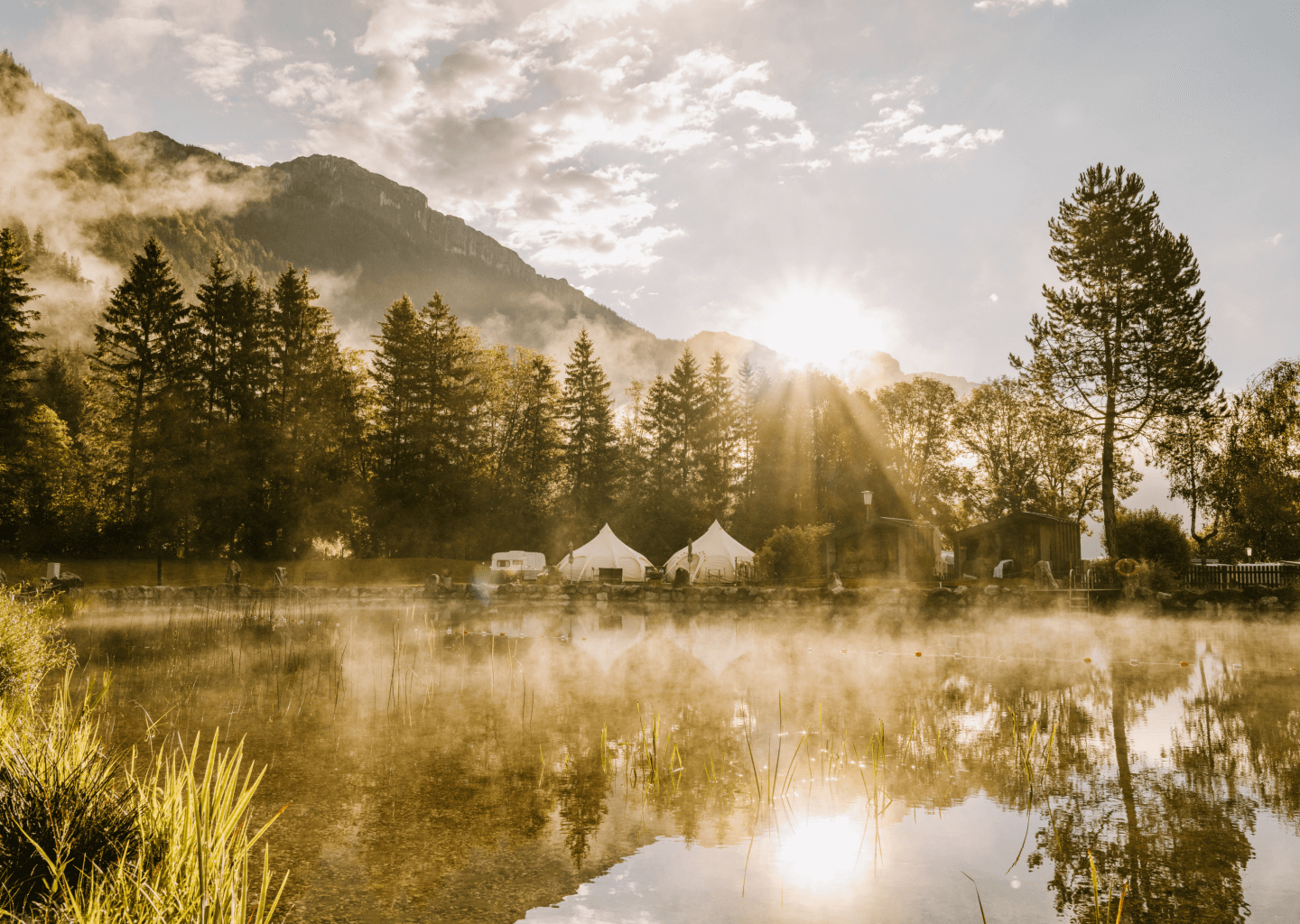 Het meer van Camping Steinplatte in de avondzon met de Alpen eronder en glampingtenten